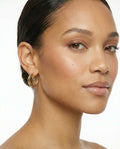 Close-up of model wearing gold ChristAdorn logo hoop earrings with a polished natural makeup look on a white background