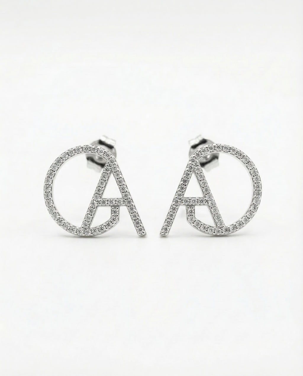 Silver pavé ChristAdorn logo stud earrings with circular and letter-shaped design on a white background.