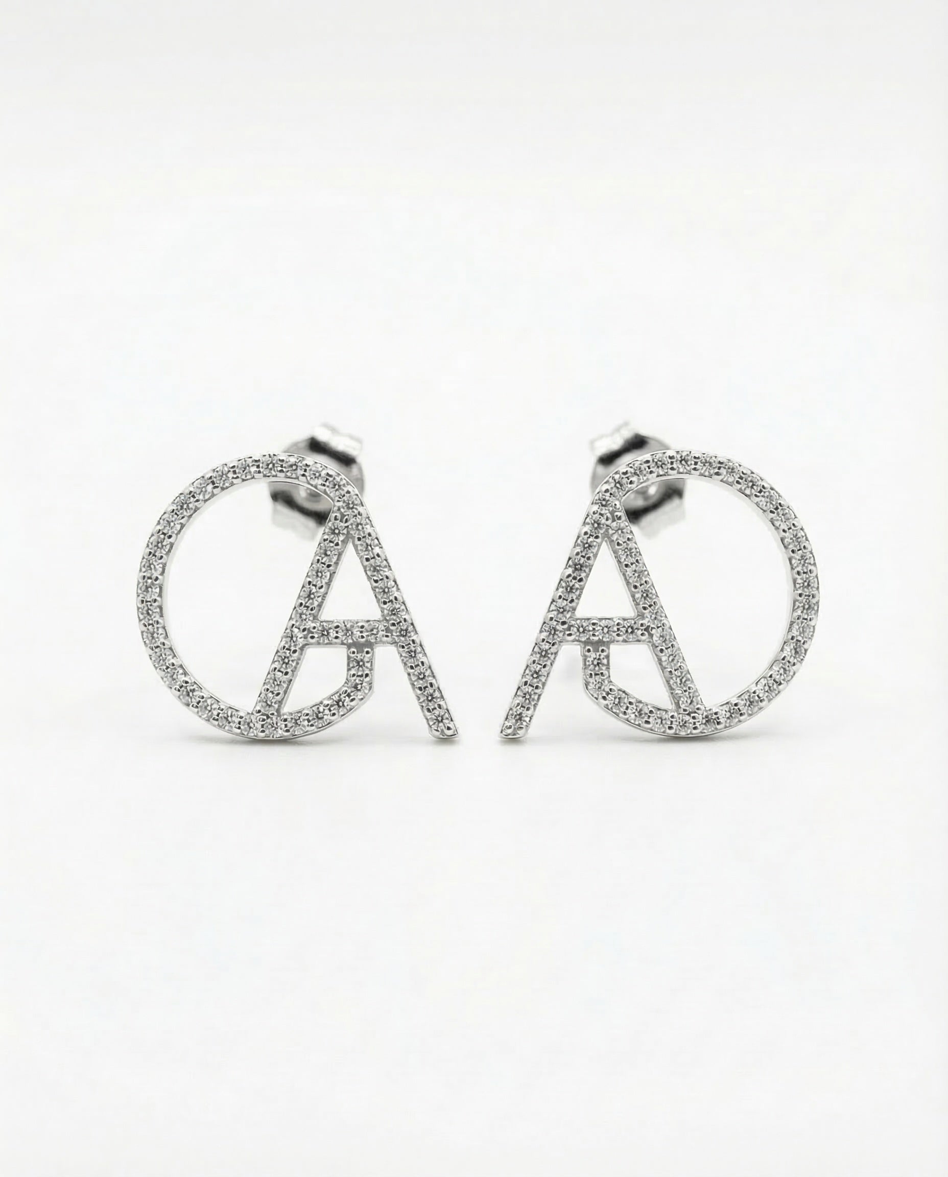 Silver pavé ChristAdorn logo stud earrings with circular and letter-shaped design on a white background.