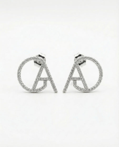 Silver pavé ChristAdorn logo stud earrings with circular and letter-shaped design on a white background.